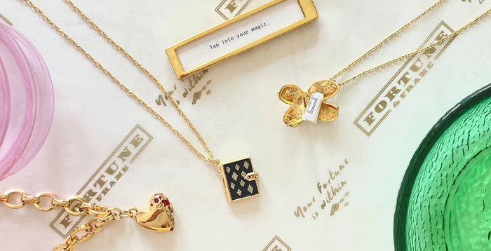 Jeweled Heart Bracelet, Onyx Stardust Book Locket, Gold Fortune Frame, and Gold Fortune Cookie Locket laid out on Fortune & Frame gift wrap.